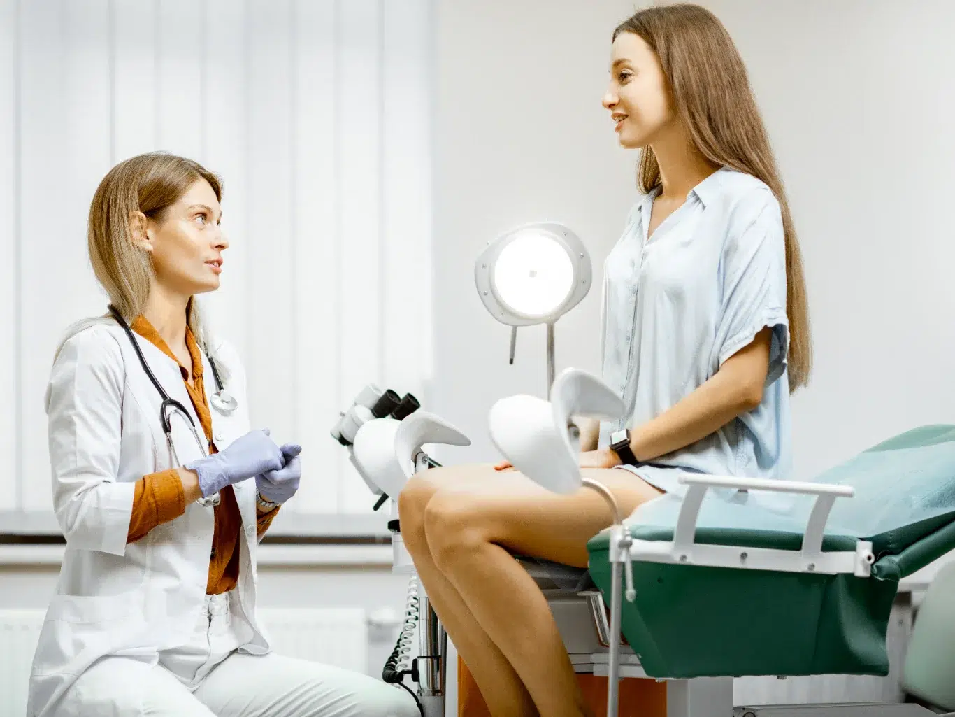 woman talking to her primary care doctor in exam room Gynecologist preparing for an examination procedure for a pregnant woman